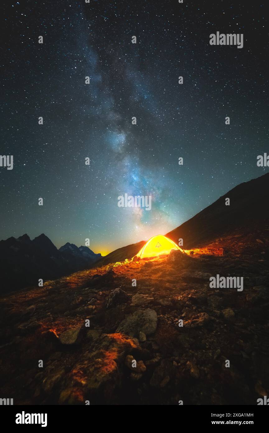 Una foto verticale del cielo stellato in cima alle montagne. La via lattiginosa satura indica una tenda luminosa in alto sulle montagne contro il Foto Stock