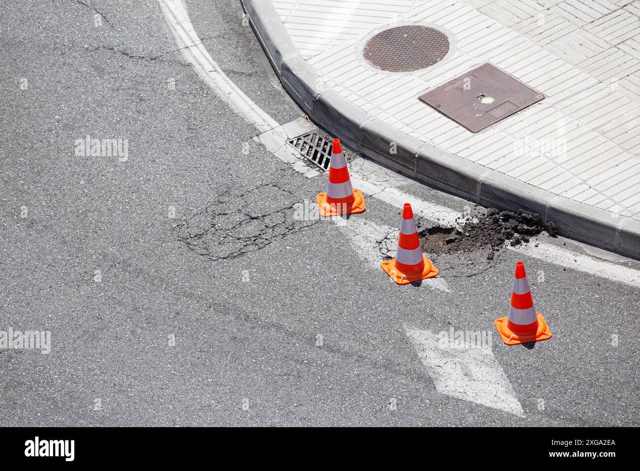 Strada urbana danneggiata contrassegnata con coni in attesa di riparazione Foto Stock