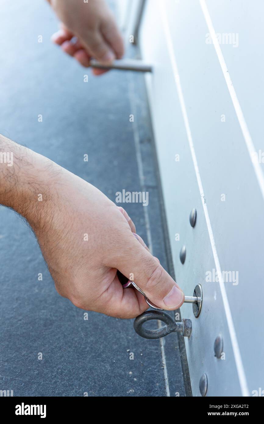 Primo piano di una mano con una chiave che chiude lo sportello dell'otturatore a rullo di un negozio. Concetto di chiusura Foto Stock