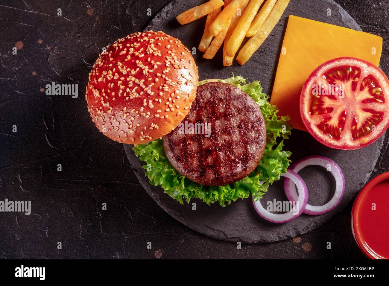 Ingredienti per hamburger di manzo, shot superiore. Bistecca di hamburger con un panino di sesamo, pomodoro, formaggio e patatine fritte Foto Stock