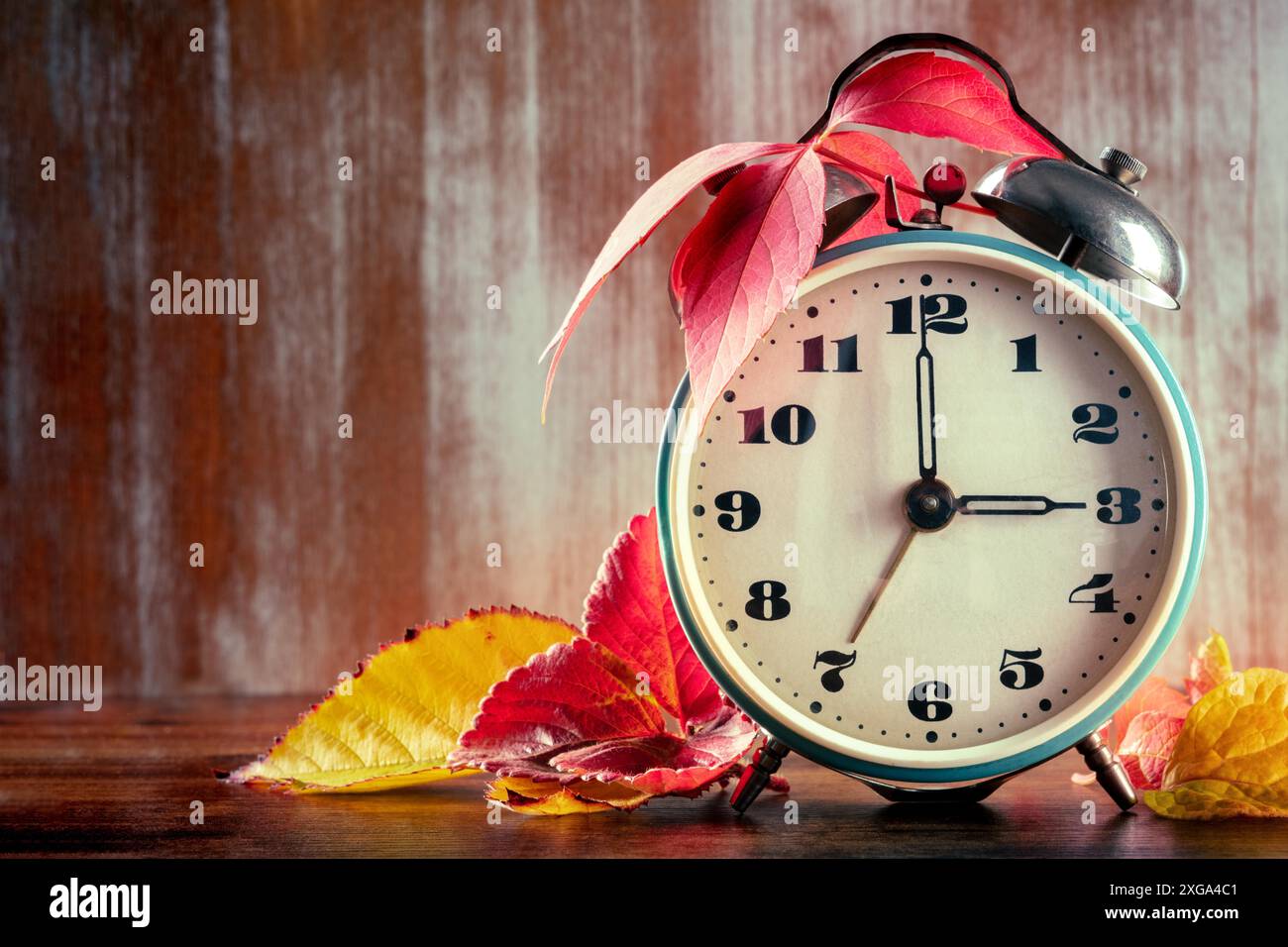 Concetto di ora legale, ritorno in autunno, con un posto per il testo. Una sveglia d'epoca con foglie d'autunno su un rustico sfondo di legno con Foto Stock
