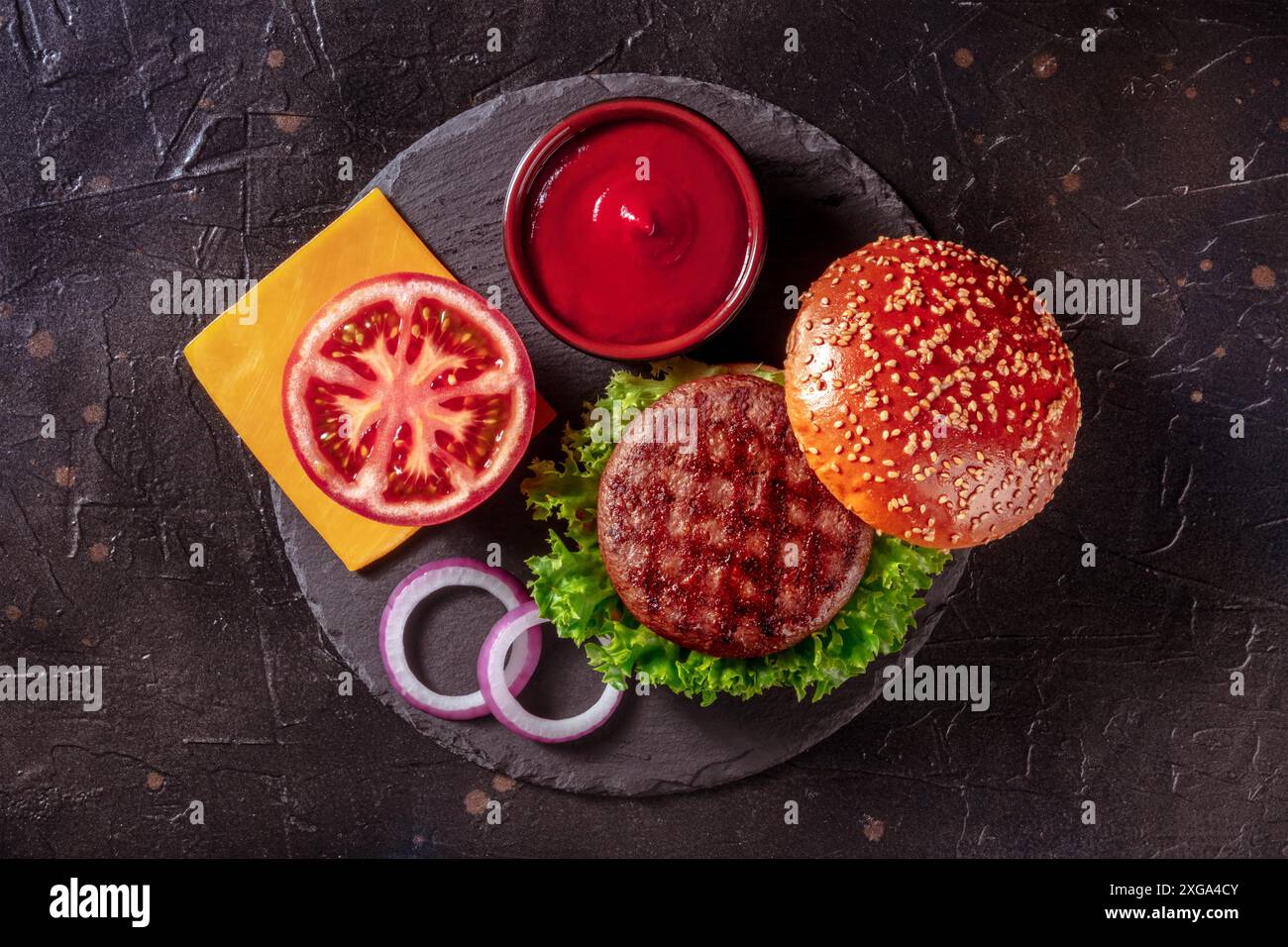 Ingredienti Burger, scatto su sfondo nero. Bistecca di manzo con verdure, formaggio e ketchup Foto Stock