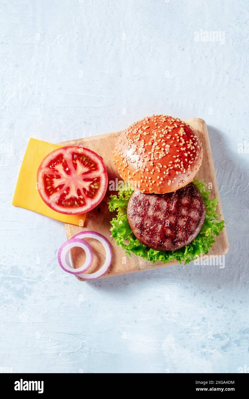 Ingredienti di hamburger, sparati dall'alto con un posto per il testo. Hamburger di manzo, pomodoro, formaggio, cipolla, insalata a foglia e pane di sesamo Foto Stock