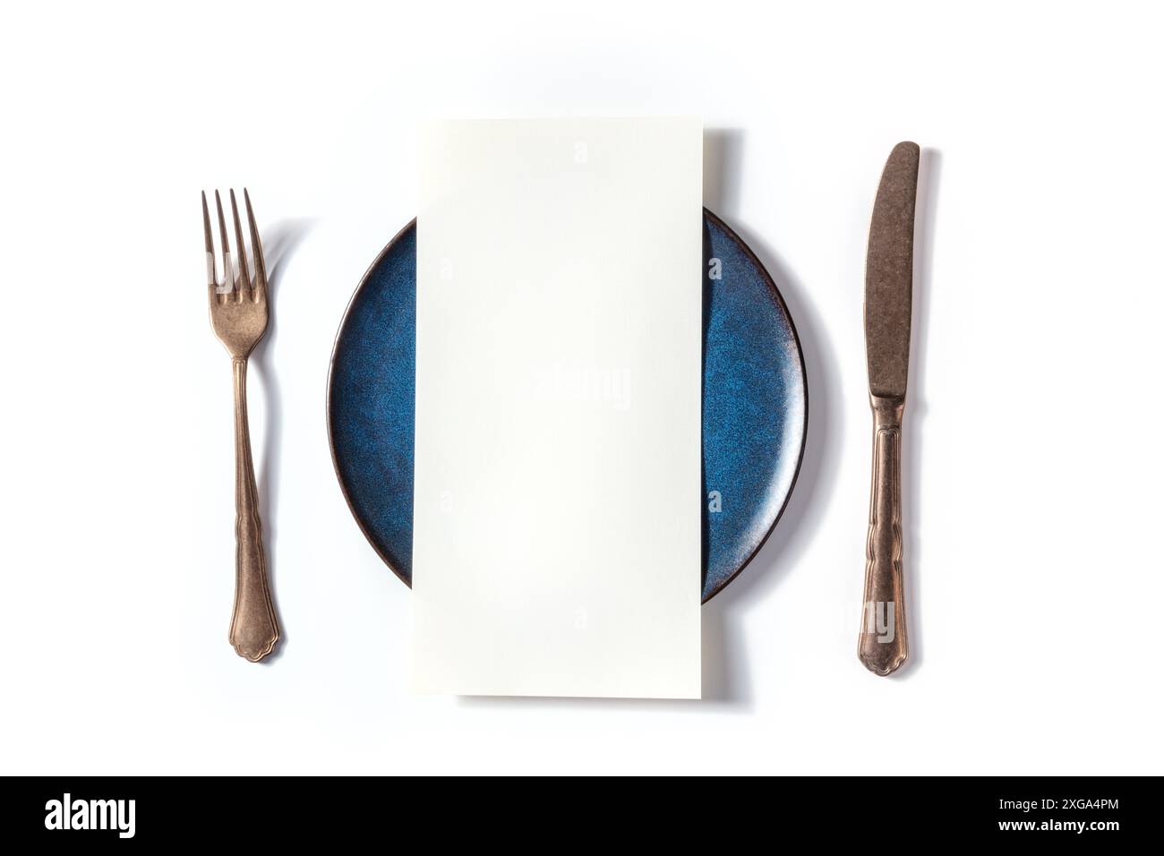 Menu per la cena o concetto di invito. Un pezzo di carta su un tavolo, con una forchetta, un coltello, e un piatto blu, sopra piano stay shot su uno sfondo bianco Foto Stock