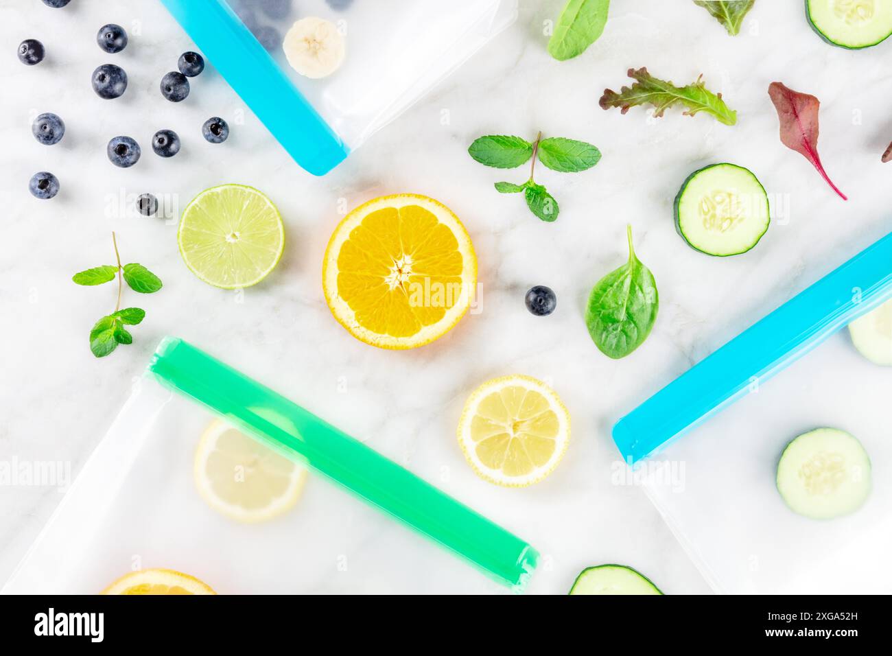 Sacchetti per la conservazione degli alimenti con frutta fresca estiva e verdure, sparati dall'alto su un tavolo da cucina in marmo bianco. Prodotti estivi in contenitori con chiusura a zip Foto Stock