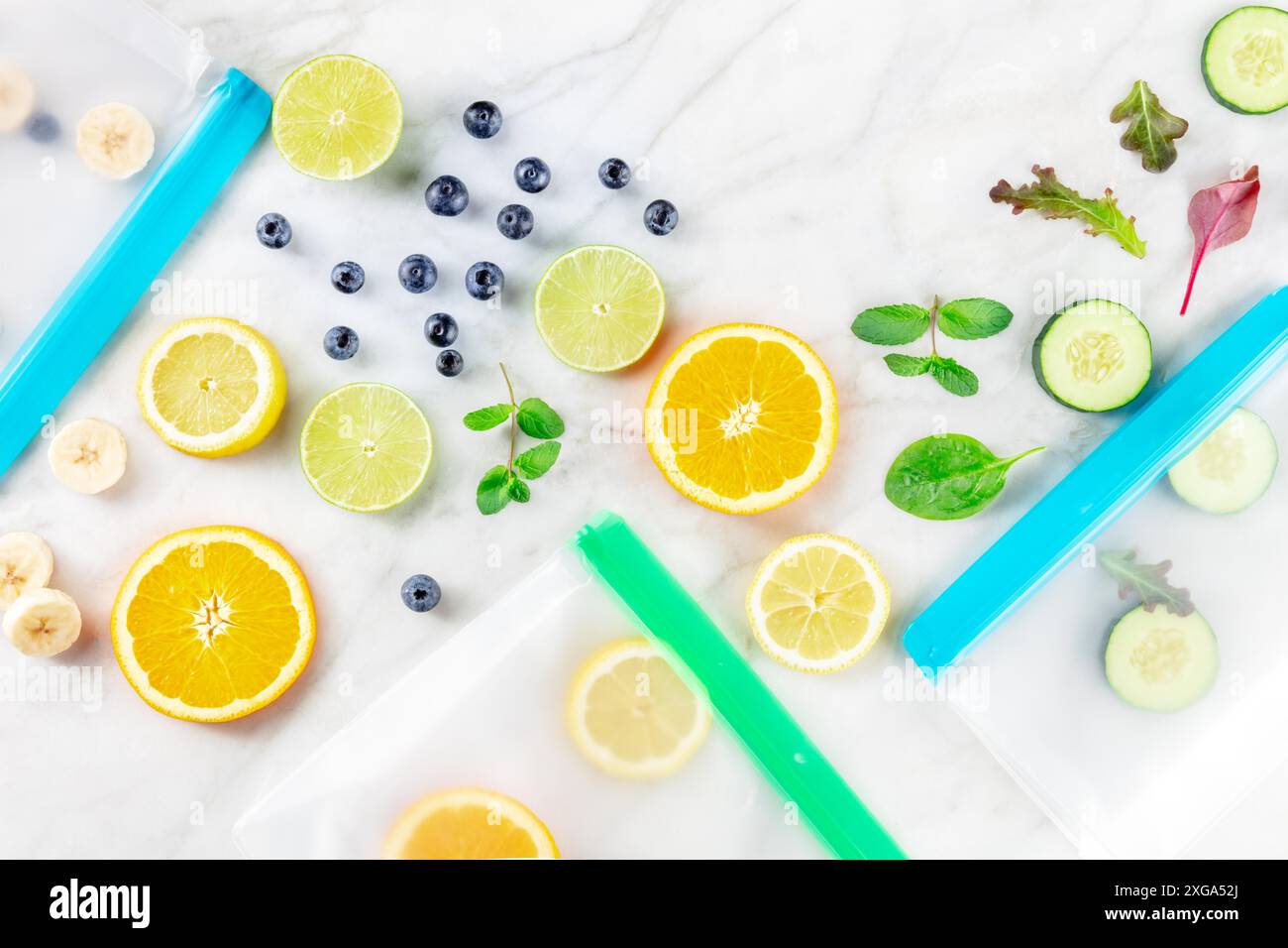 Sacchetti riutilizzabili per la conservazione degli alimenti con frutta e verdura, posate a soffitto su un tavolo da cucina in marmo bianco. Prodotti freschi estivi in ziplock Foto Stock