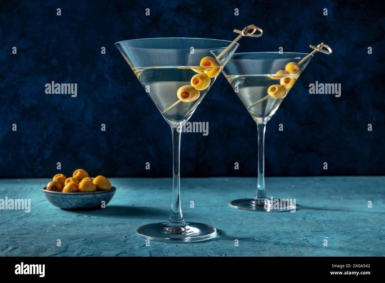 Martini, due bicchieri con olive speziate. Cocktail alcolico su sfondo blu Foto Stock