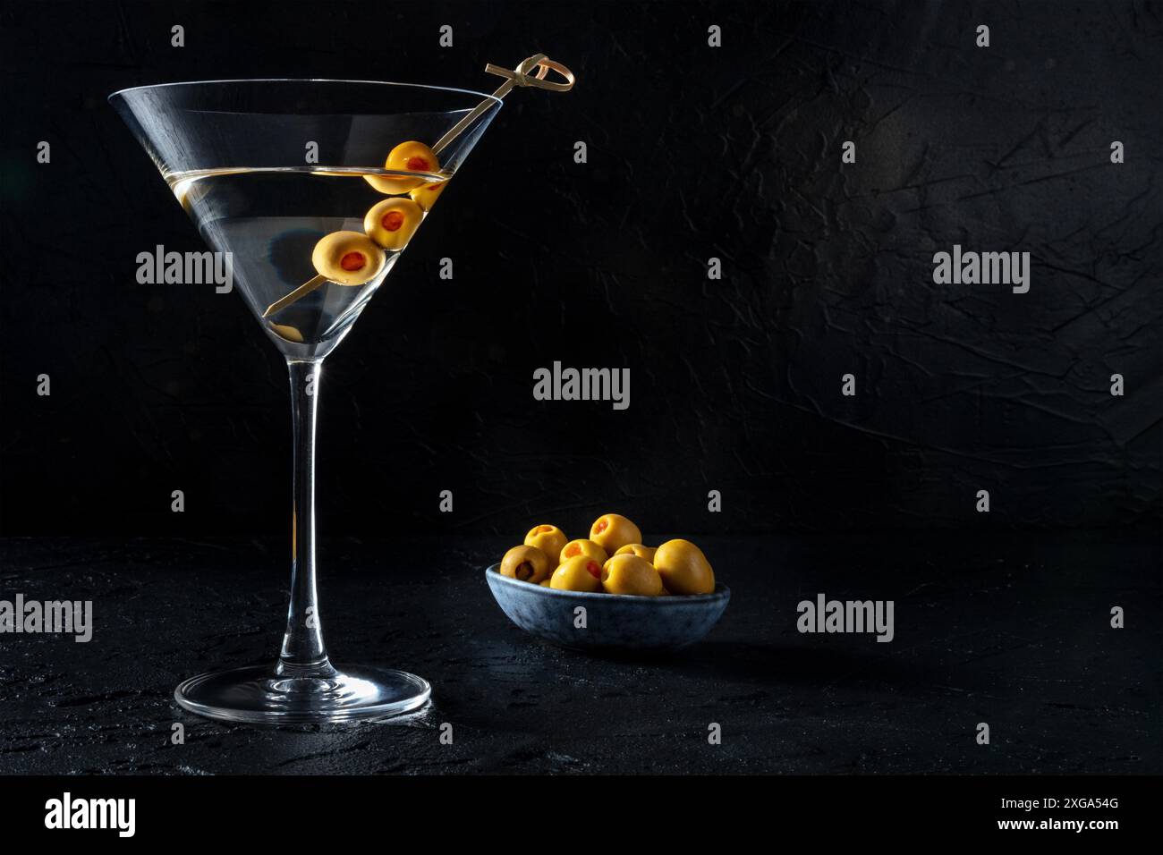 Martini, un bicchiere con olive speziate su stuzzicadenti, su fondo nero. Cocktail alcolico con posto per testo Foto Stock