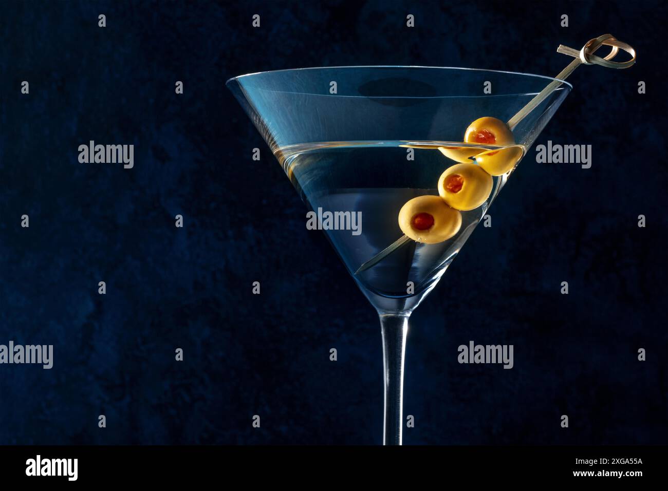 Martini, un bicchiere con olive speziate su stuzzicadenti, su fondo scuro. Cocktail alcolico con spazio copia Foto Stock