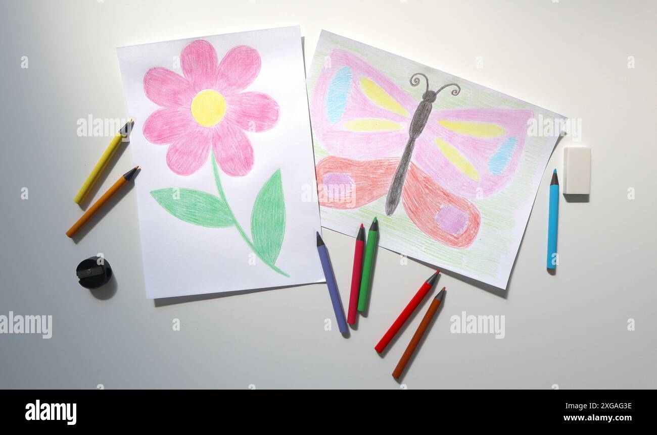Foto di disegni per bambini con matite colorate. Uno mostra fiori, l'altro farfalla. Nelle vicinanze sono presenti matite colorate, una gomma e un affilatore. Foto Stock