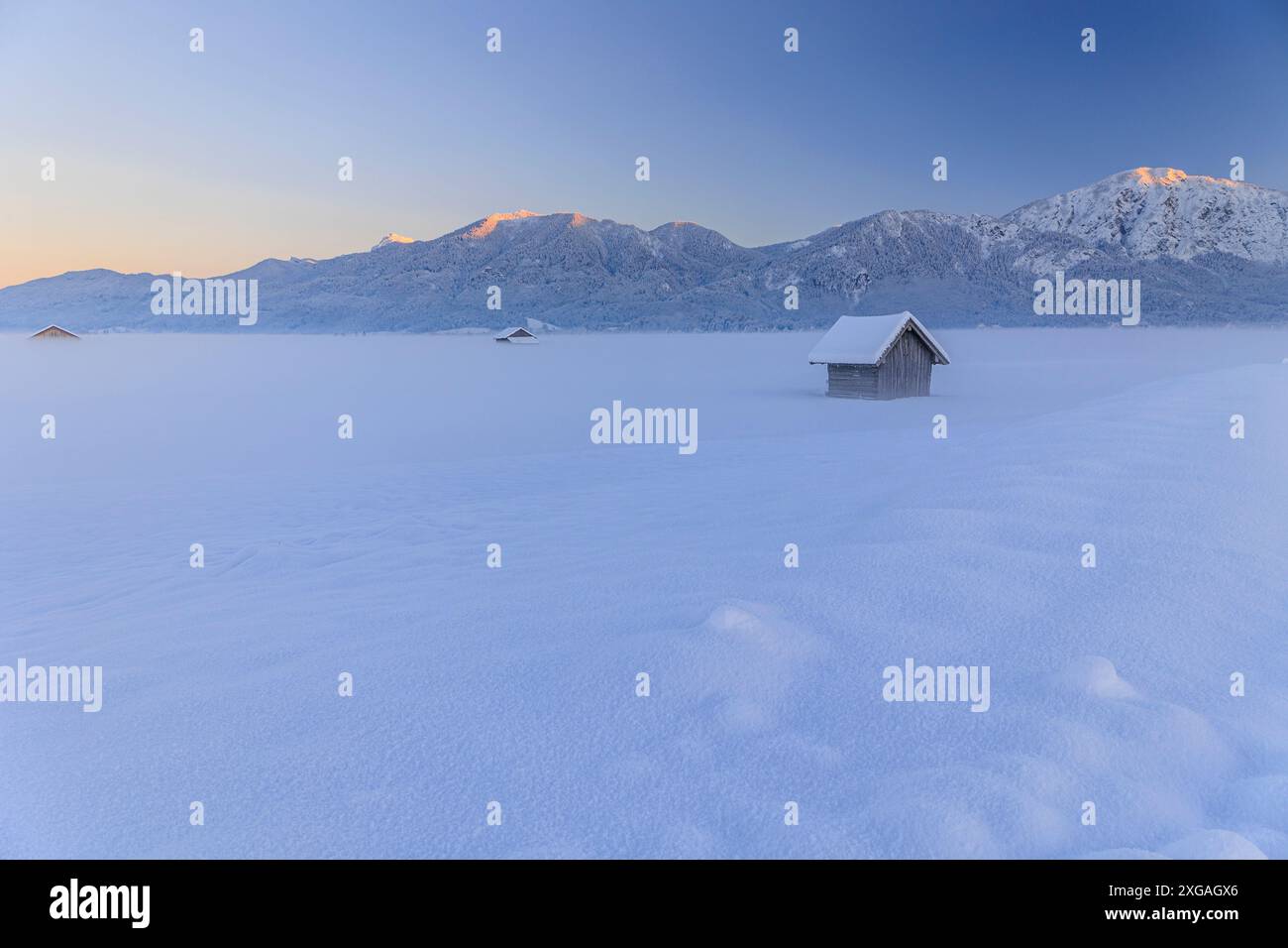 Capanna in legno al tramonto di fronte alle montagne, inverno, Loisach-Kochelsee-Moor, vista su Rabenkopf e Jochberg, Baviera, Germania, Europa Foto Stock