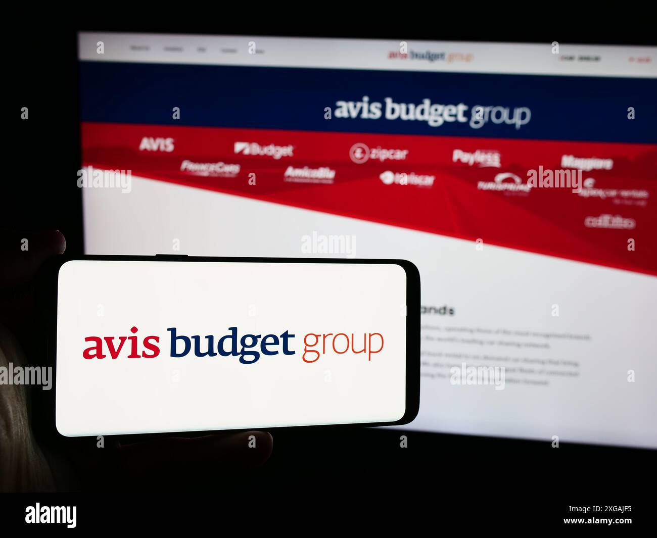 Persona che possiede uno smartphone con il logo della società di noleggio auto statunitense Avis budget Group Inc. Davanti al sito Web. Mettere a fuoco il display del telefono. Foto Stock