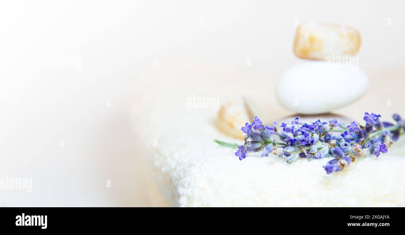 Una pila di morbidi asciugamani bianchi con fiori di lavanda e una pila di pietre bilanciate, creando un'atmosfera spa e simile a dzen. Foto Stock