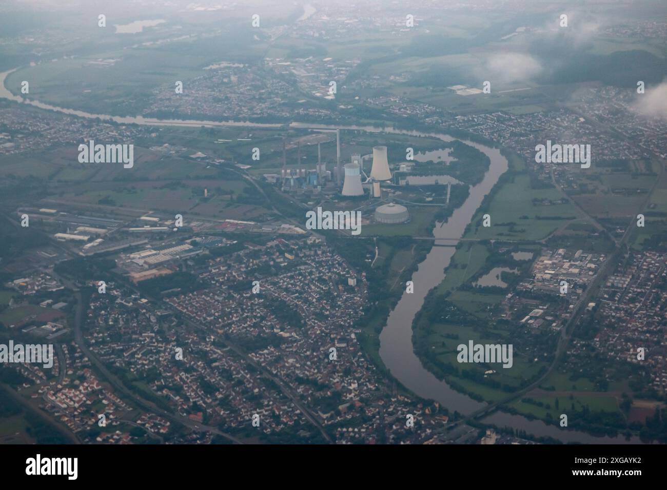 Una città con fiume e centrale elettrica è vista dall'alto con un'atmosfera nebulosa. Il cielo è blu e la città è piena di edifici. Foto Stock