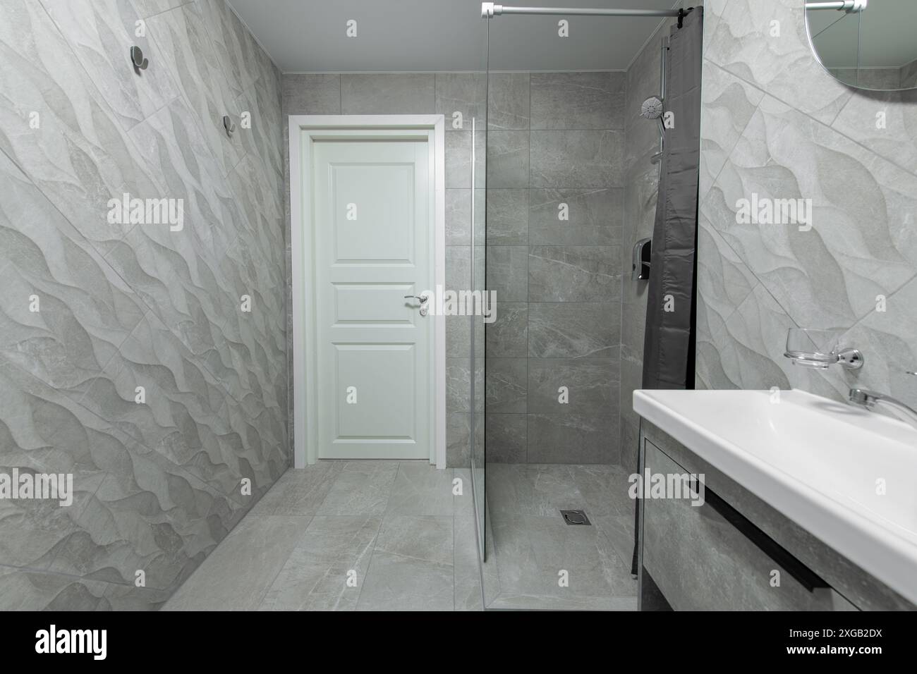 Bagno luminoso, elegante, moderno e minimalista. Design interno della doccia con porta bianca, pareti in mattonelle grigie, doccia, lavandino Foto Stock