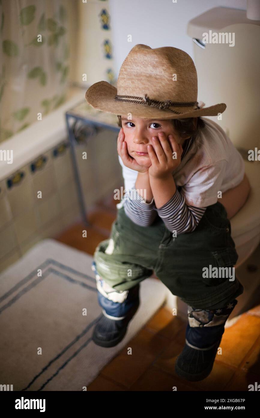 Un bambino di tre anni si siede in bagno con un cappello da cowboy e stivali gonfiabili a San Miguel de Allende, Messico. Foto Stock