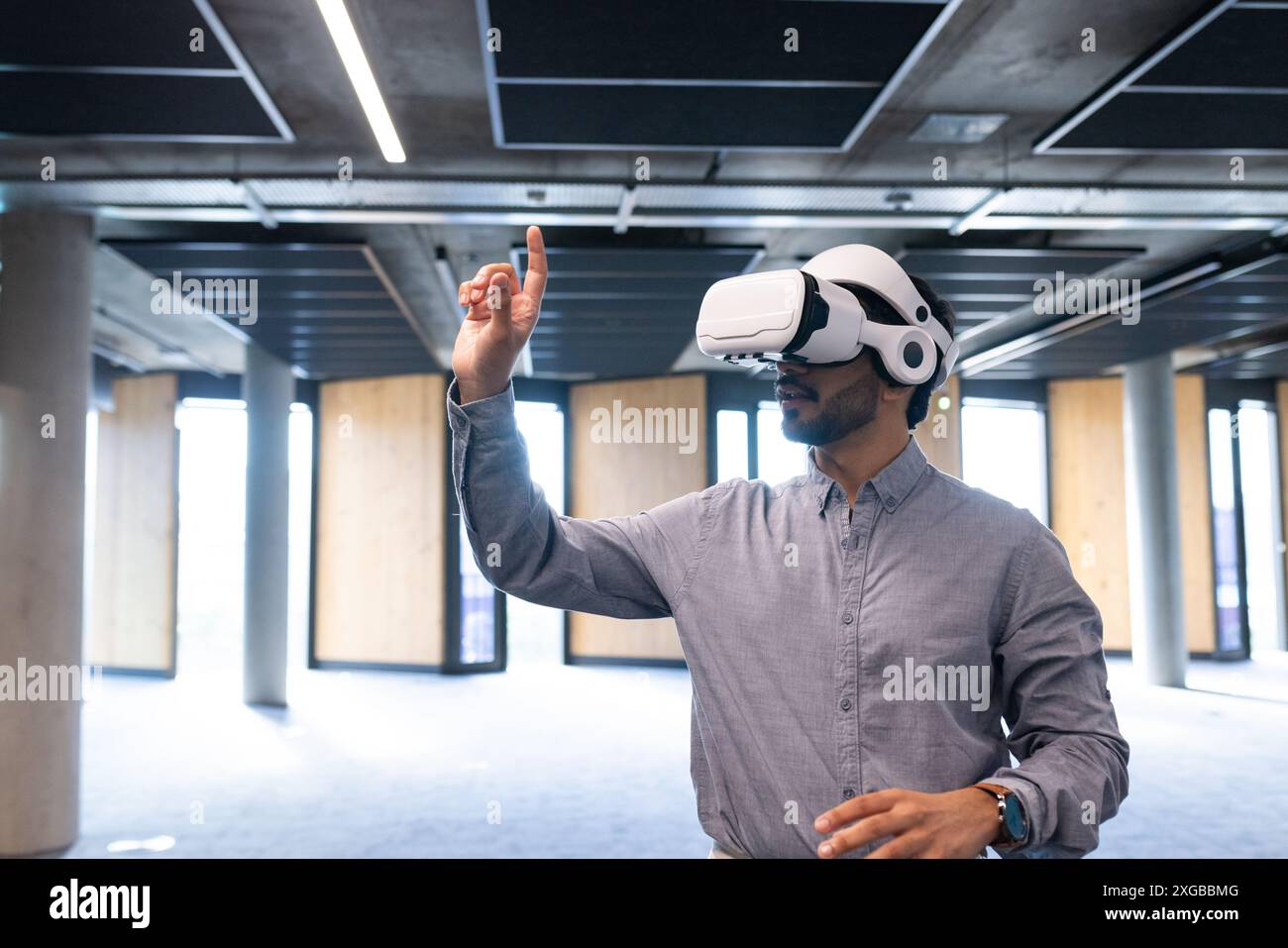 Utilizzando il visore VR, l'uomo interagisce con l'interfaccia virtuale in un ufficio moderno, copia spazio Foto Stock