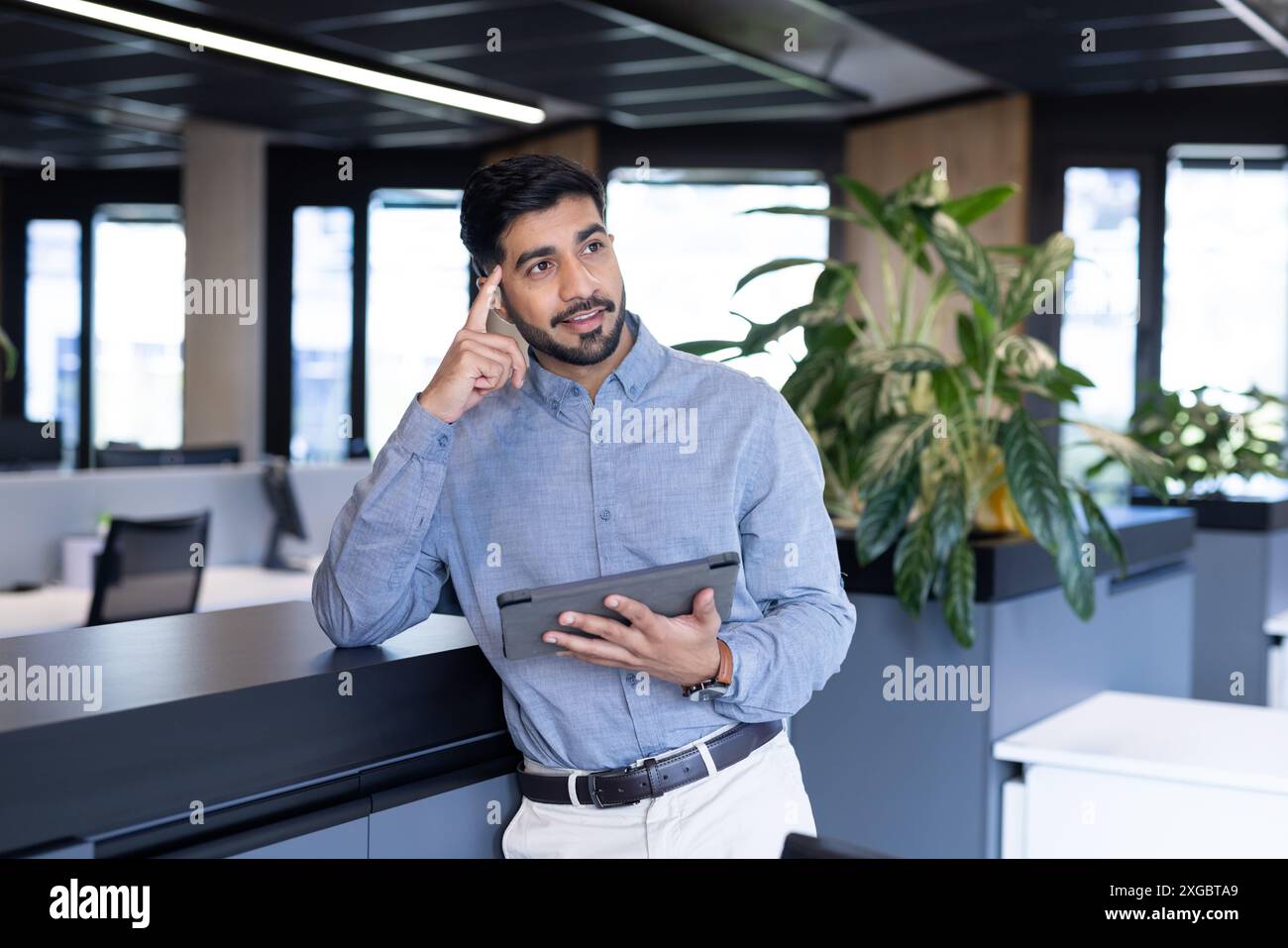 Tenendo un tablet e pensando, uomo in un ambiente d'ufficio moderno Foto Stock
