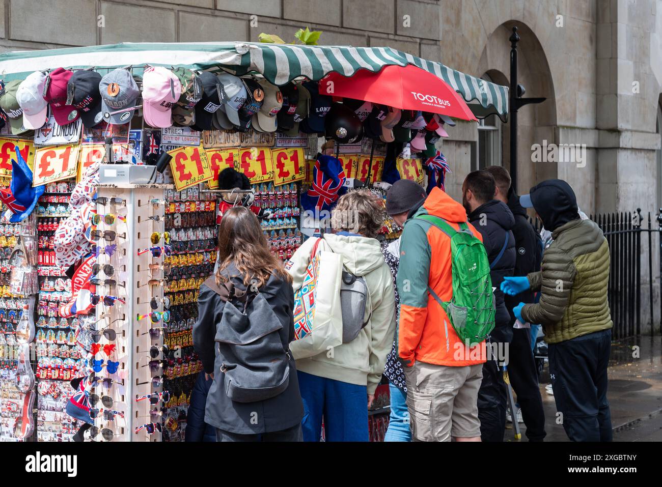 Turisti intorno a una bancarella di souvenir a Whitehall, Londra, in un giorno d'estate piovoso. Cappelli, cappelli, occhiali da sole, portachiavi, magneti per frigo. Persone che visualizzano i prodotti Foto Stock