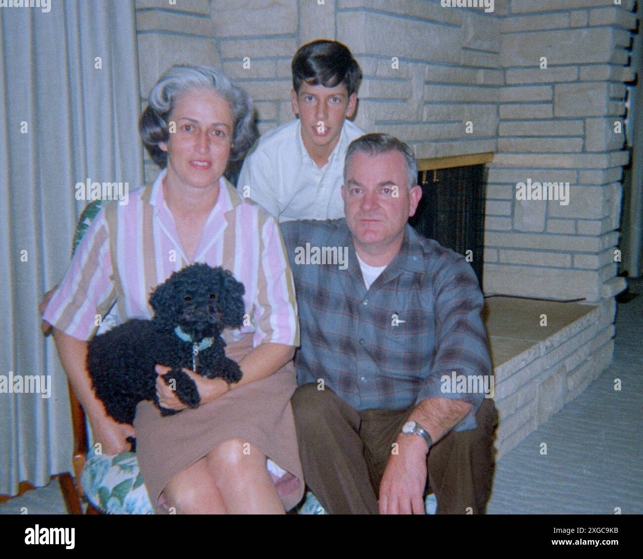 La famiglia posa davanti al loro caminetto con il loro barboncino per animali, 1969. Santa Rosa, CALIFORNIA, Stati Uniti, 1969 Foto Stock