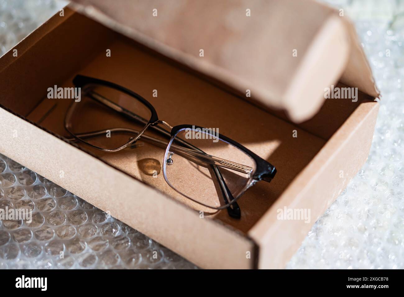 Un paio di occhiali da vista in una scatola di cartone marrone, posizionati su una pellicola a bolle d'aria. Foto Stock