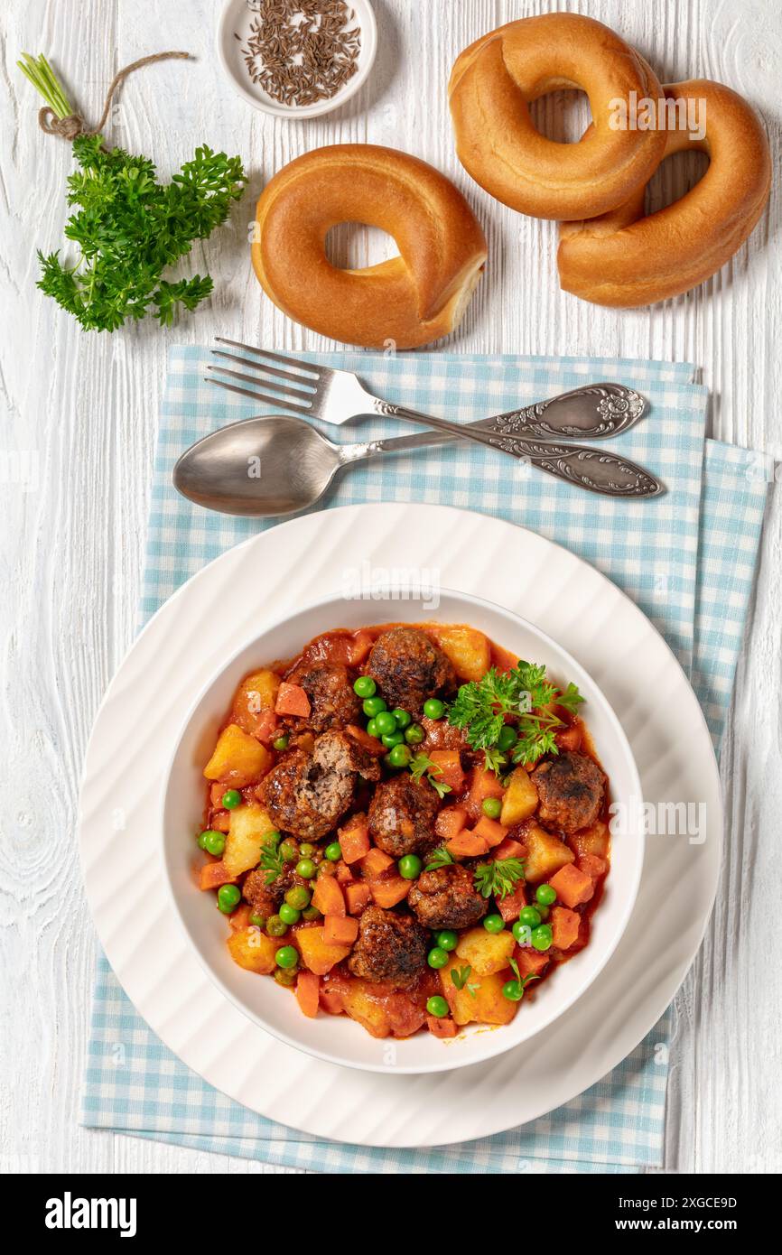 stufato turco di polpette, sulu kofte, piatto abbondante con patate, carote e piselli verdi sospesi in salsa di pomodoro servito in un recipiente con forchetta e cucchiaio su w. Foto Stock