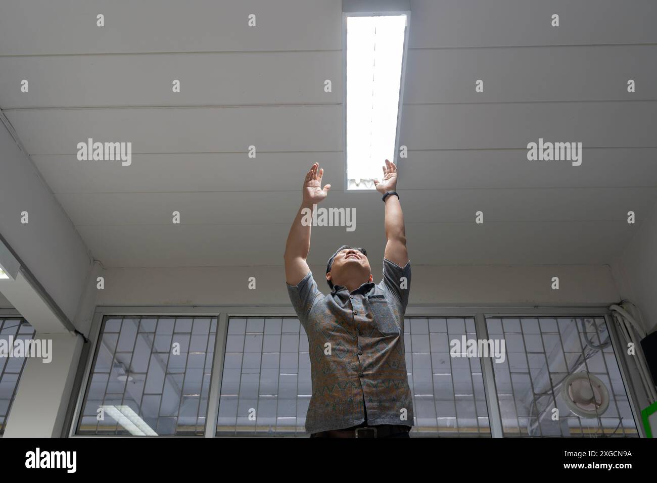 Lampadina a risparmio energetico per scatti ad angolo elevato in una lampada bianca sul soffitto, che controlla o sostituisce le luci fluorescenti negli edifici. Uomo felice che cambia a l Foto Stock