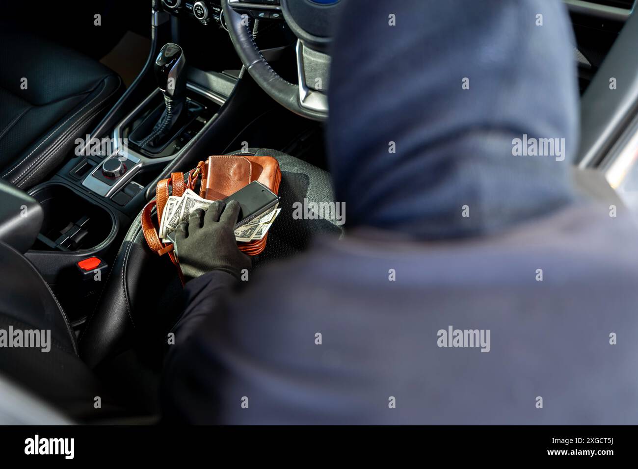 Una mano che tira fuori un portafoglio dal sedile del passeggero di un'auto. Le cose personali di valore lasciate sul sedile anteriore sono facili da catturare per i ladri. Thiev Foto Stock