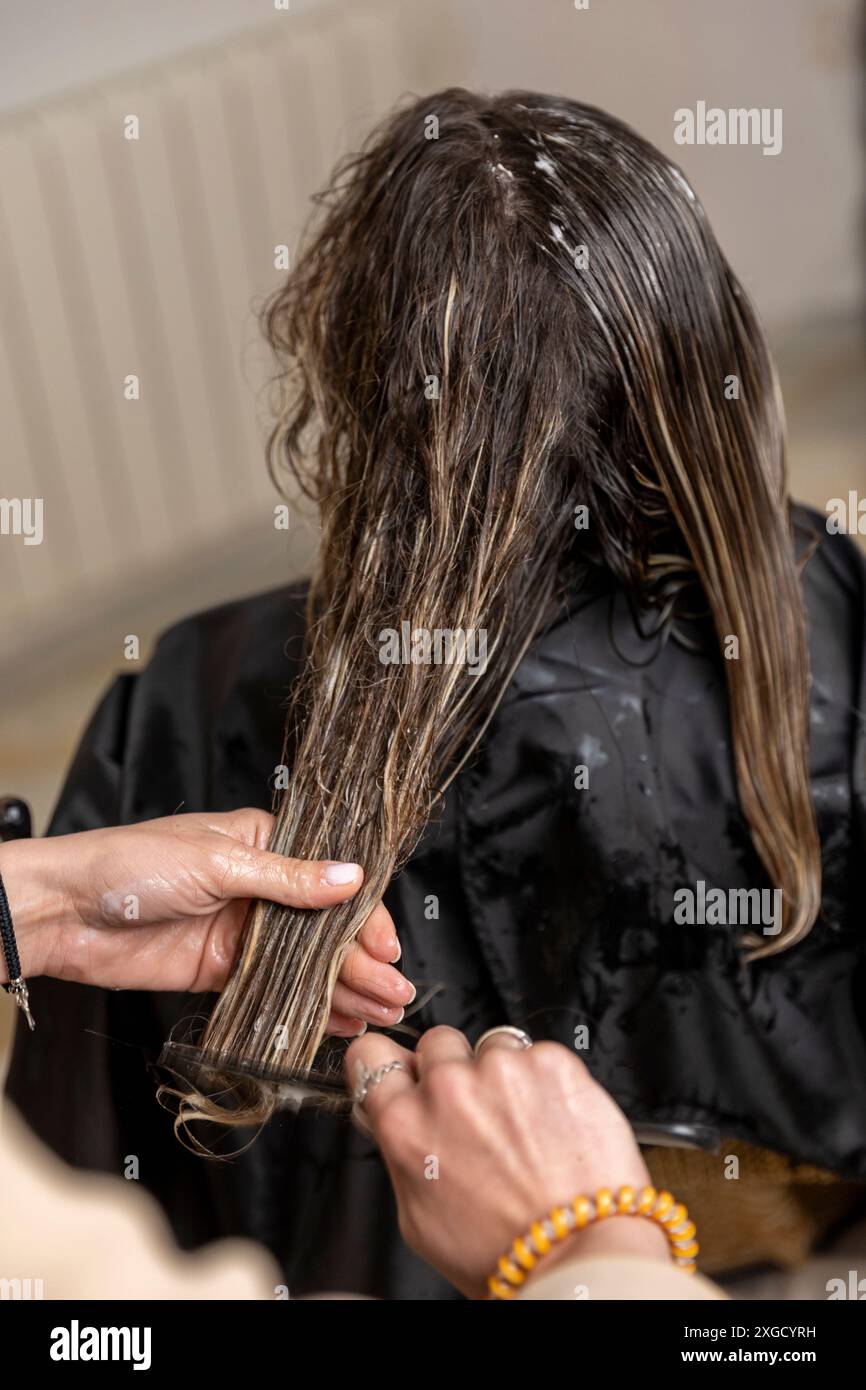 Donna con capelli ricci castani che riceve una delizia dal parrucchiere. Stile di vita Foto Stock