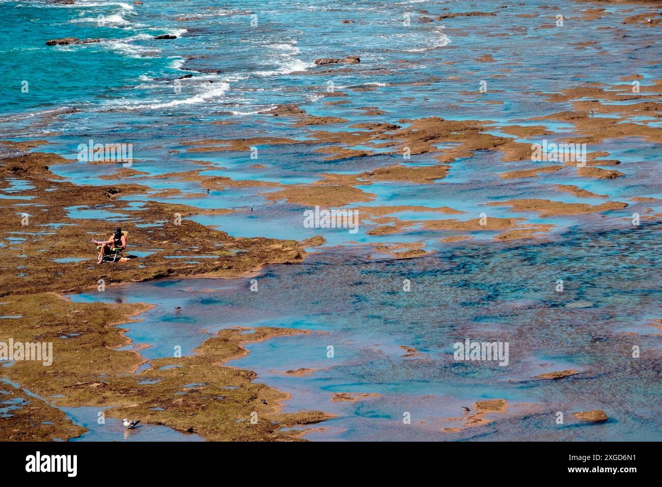 Cádiz, Spagna - 14 aprile 2024: Una persona, non identificabile, apprezza una giornata in spiaggia, seduta su una sedia incastonata tra rocce e mare a la Caleta Foto Stock