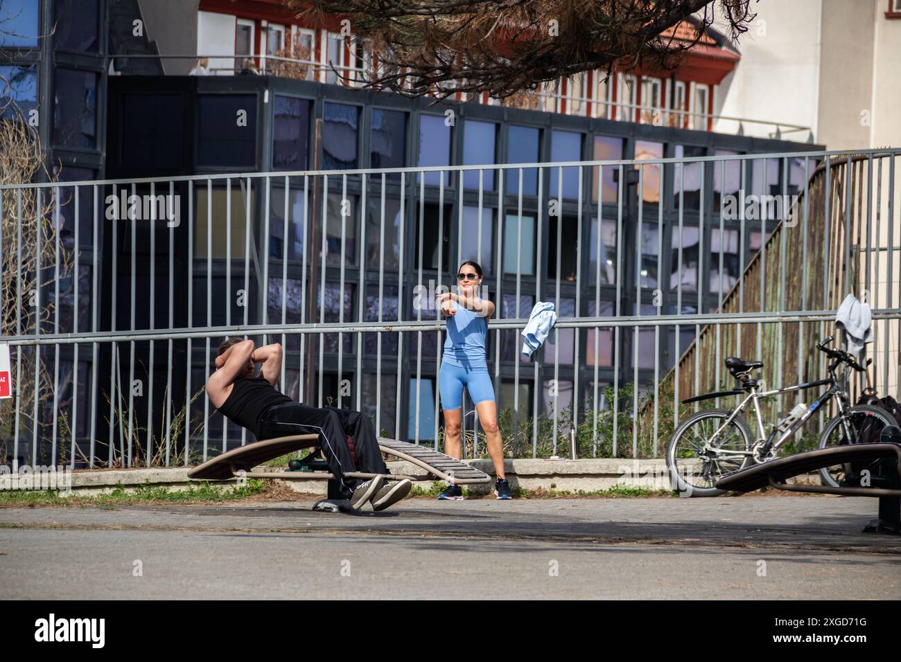 Un parco pubblico con attrezzature sportive, una ragazza e un uomo si allenano e si sgranchiscono all'aria aperta, godendosi lo spazio aperto mentre si svolgono attività sportive Foto Stock