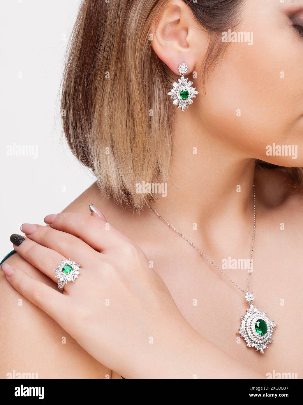 Donna elegante che indossa uno squisito set di gioielli color smeraldo e diamanti che include una collana, orecchini e un anello. Foto Stock