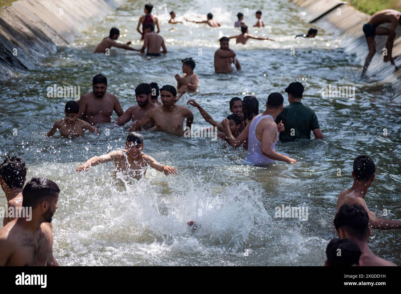 I residenti del Kashmir hanno visto nuotare in un canale d'acqua durante una giornata calda a Pulwama. Quest'anno il Kashmir ha affrontato sfide climatiche senza precedenti, segnate da temperature massime record a Srinagar e in tutta la regione. Gli esperti attribuiscono questi eventi meteorologici estremi agli impatti più ampi del cambiamento climatico. I cambiamenti nei modelli monsonici e la presenza irregolare di disturbi occidentali hanno interrotto i cicli meteorologici tradizionali della regione, portando a precipitazioni irregolari e fluttuazioni di temperatura. Questi cambiamenti non solo influenzano i modelli agricoli e le risorse idriche, ma anche pongono segni Foto Stock