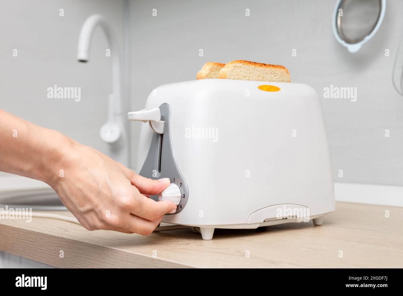 casalinga che imposta il timer sul tostapane. casalinga che frigge il pane in un tostapane, in cucina. donna che fa un brindisi. pane per toast. tosta il pane in un Foto Stock