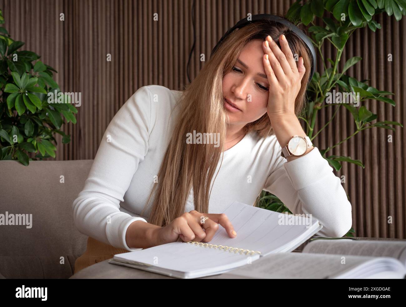 Una donna con le cuffie sembra stressata mentre studia, tiene la testa e punta un notebook. Foto Stock
