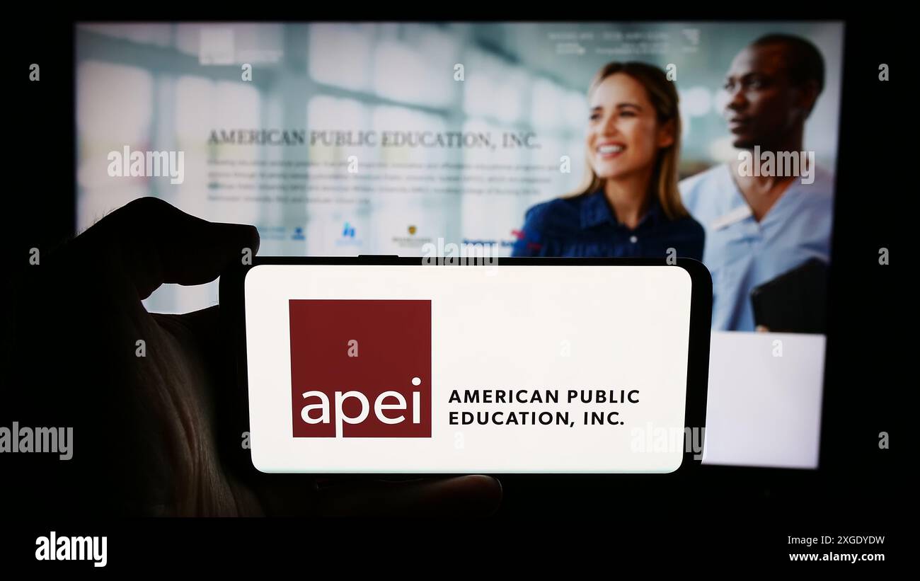 Persona che possiede uno smartphone con il logo della società statunitense American Public Education Inc. (APEI) davanti al sito Web. Mettere a fuoco il display del telefono. Foto Stock