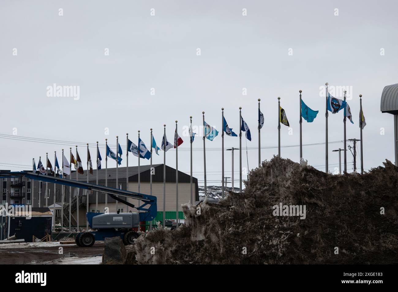 Bandiere inuit che sventolano dietro l'Assemblea legislativa del Nunavut sulla strada federale a Iqaluit, Nunavut, Canada Foto Stock