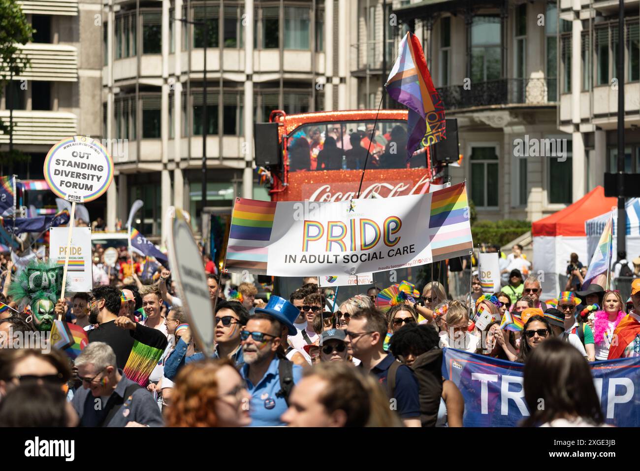 Una folla di persone che camminano lungo Park Lane alla London Pride Parade 2024, con un enorme striscione arcobaleno che recita Pride in Adult Social Care. REGNO UNITO Foto Stock