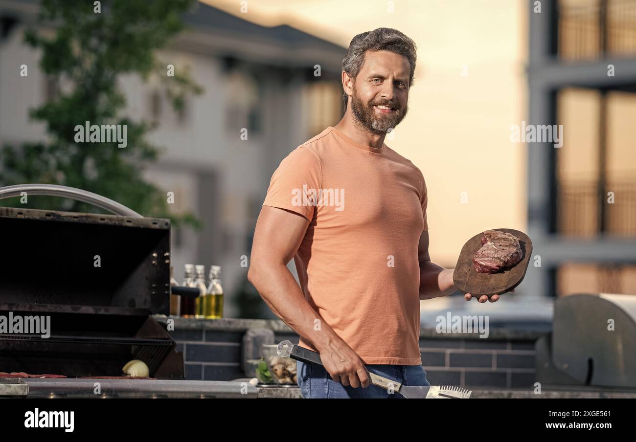 Uomo che si diverte a fare barbecue. Preparazione alla griglia con guru affumicato. uomo che grigia le sue carni preferite. cuoco che mostra le sue tecniche di barbecue durante l'evento di cucina Foto Stock