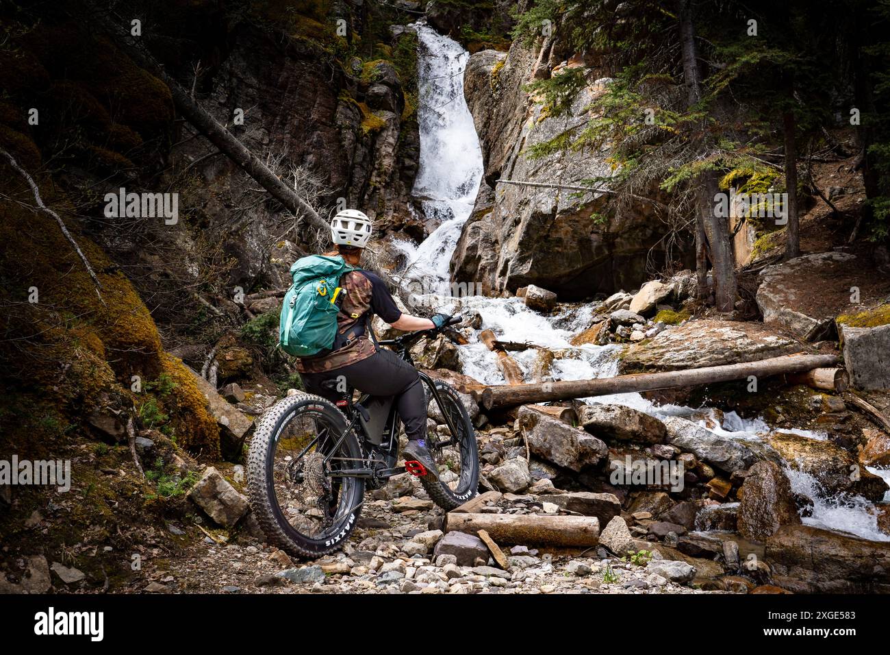 Lake Louise, Alberta Canada, 24 giugno 2024: Mountain Biker fa una pausa ammirando una cascata lungo il sentiero del lago Ross nel Banff National Park. Foto Stock
