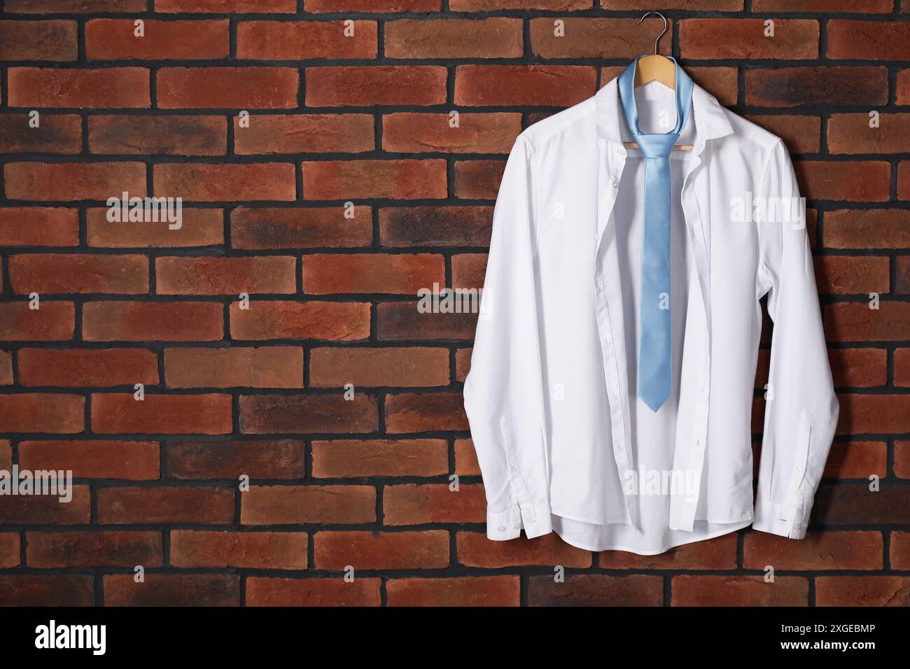 Appendiabiti con camicia bianca e cravatta azzurra sulla parete in mattoni rossi. Spazio per il testo Foto Stock
