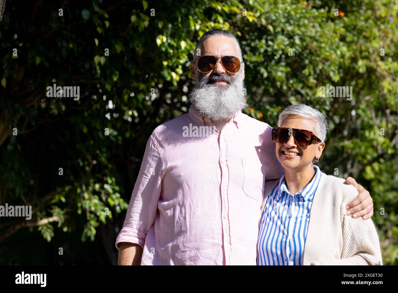 Coppia senior che indossa occhiali da sole, sorride e abbraccia all'aperto alla luce del sole Foto Stock