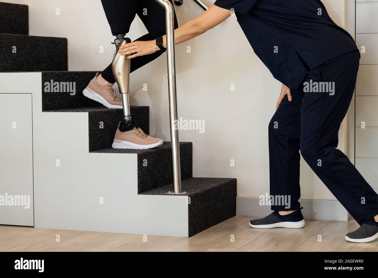 Assistere il paziente con una protesi della gamba che scende le scale nel centro di riabilitazione Foto Stock