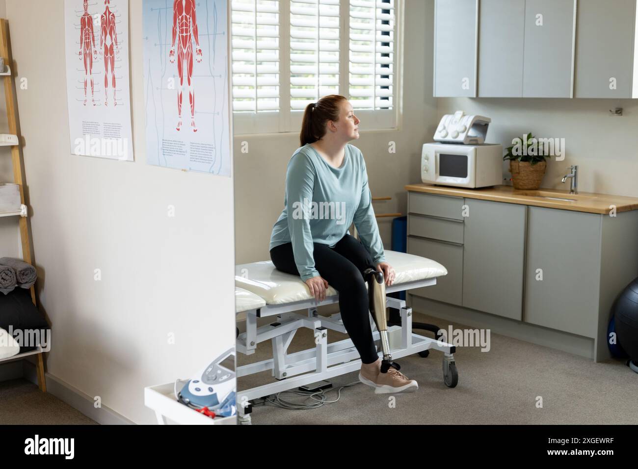 Seduta sul tavolo d'esame, donna con protesi gamba in clinica medica Foto Stock