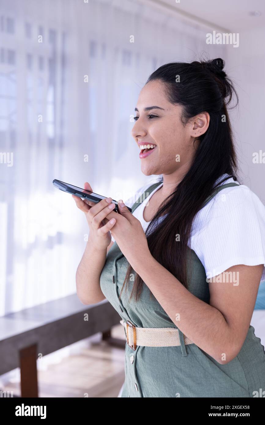 Donna sorridente che utilizza l'assistente vocale dello smartphone in un ambiente luminoso e moderno Foto Stock