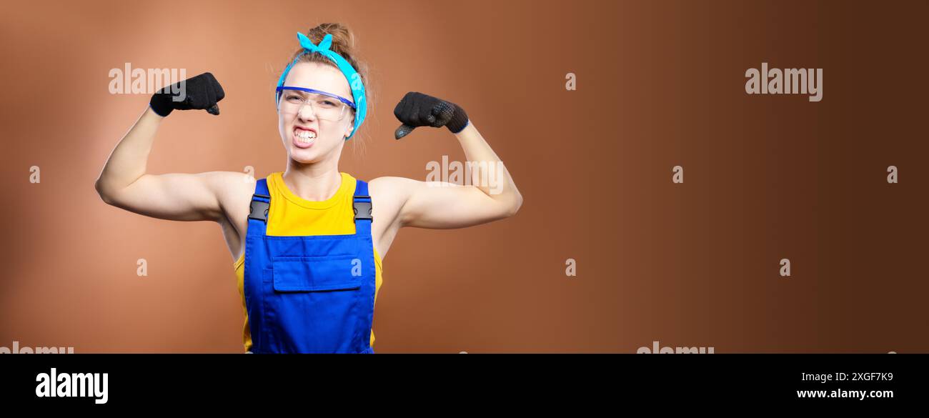 Panoramica bella donna caucasica lavoratrice riparatrice con gli occhi blu in uniforme mostrando muscoli del braccio, sorridendo orgogliosamente e facendo una forte tristezza. Il Foto Stock