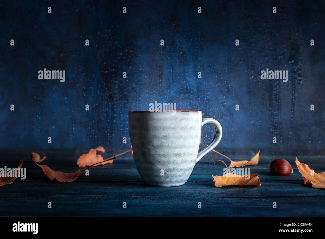 Una tazza di tè con foglie autunnali di fronte ad una finestra con la pioggia dietro di essa, con un posto per il testo Foto Stock