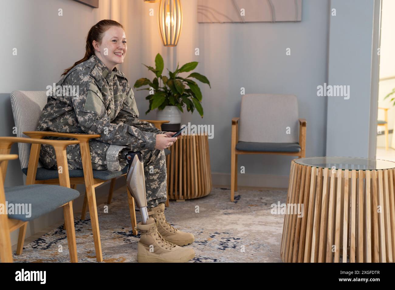 Seduta in sala d'attesa, donna in uniforme indefinita con protesi gamba sorridente, copia spazio Foto Stock