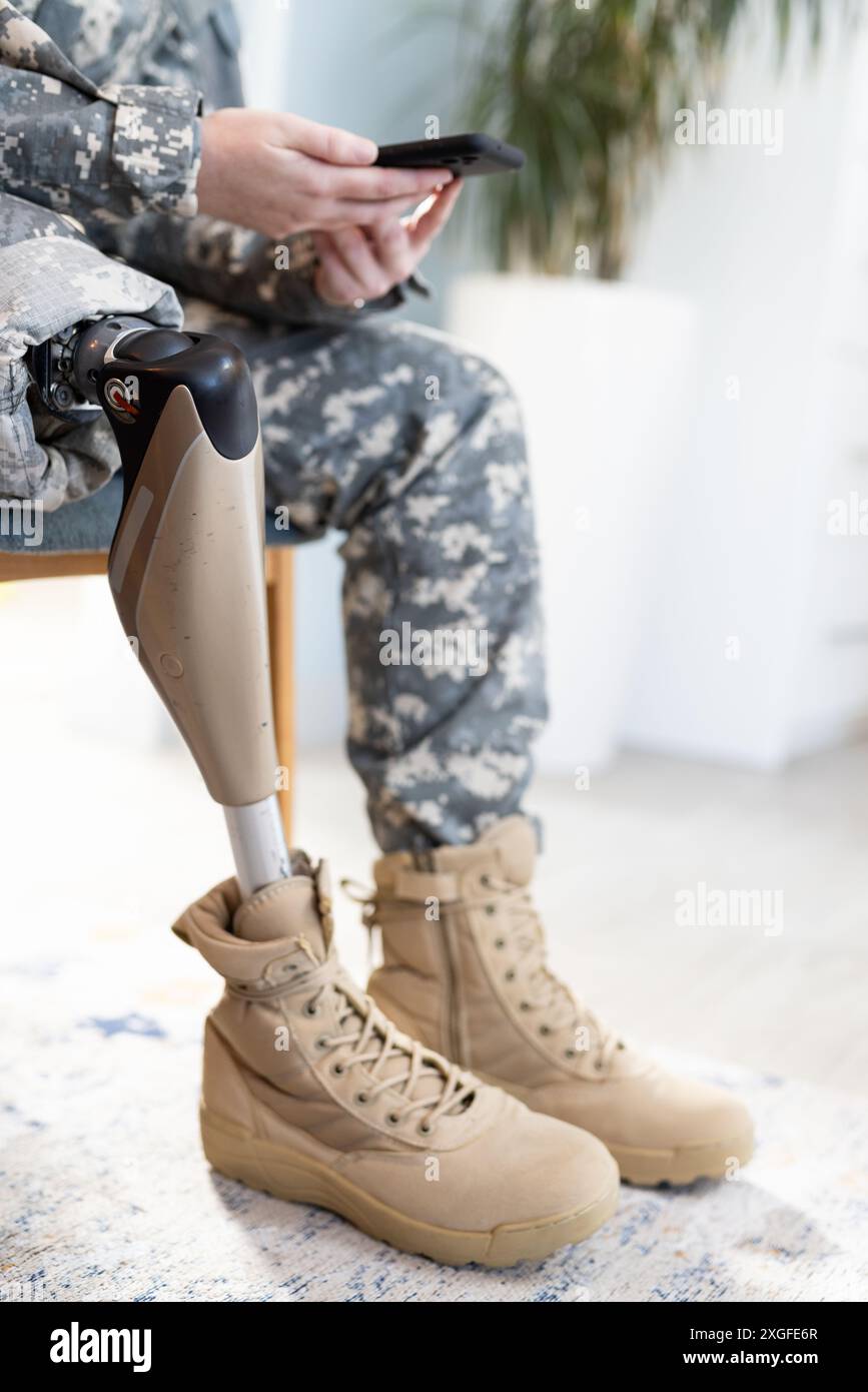 Utilizzando lo smartphone, persona in uniforme indefinita con protesi gambe sedute in casa Foto Stock