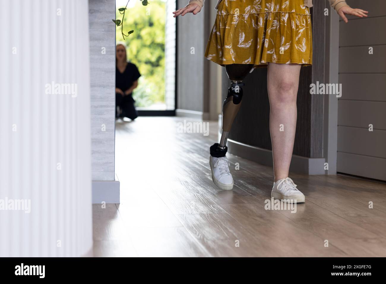 Camminare con una gamba protesica, donna con un abito giallo che pratica al chiuso, copiare spazio Foto Stock